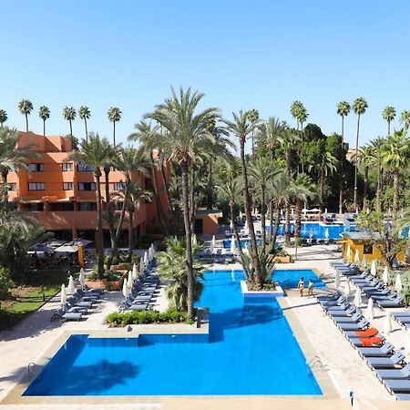 Hotel Kenzi Rose Garden Marrakesh Esterno foto The photo shows a resort-style area with several swimming pools surrounded by palm trees. The pools are clear blue and are lined with numerous lounge chairs for relaxation. There is a vibrant atmosphere, highlighted by lush greenery and a sunny sky. 