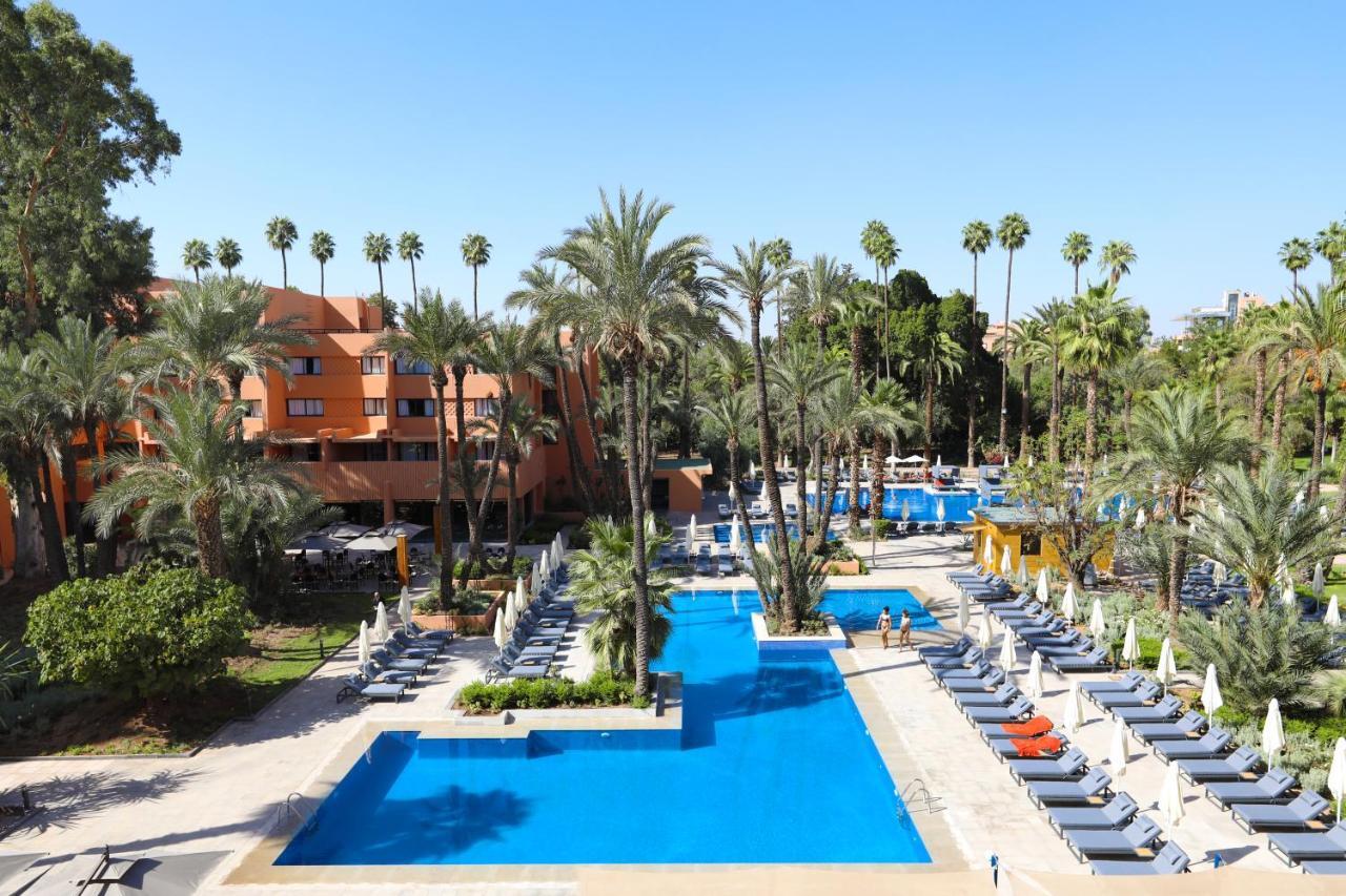 Hotel Kenzi Rose Garden Marrakesh Esterno foto The photo shows a resort-style area with several swimming pools surrounded by palm trees. The pools are clear blue and are lined with numerous lounge chairs for relaxation. There is a vibrant atmosphere, highlighted by lush greenery and a sunny sky. 
